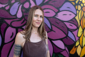 Portrait of Tara Aal standing against painted flower grafitti wall in shades of purple